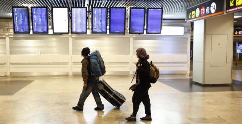 Unos jóvenes buscan su vuelo en los paneles informativos en el aeropuerto dolfo Suárez-Barajas. REUTERS