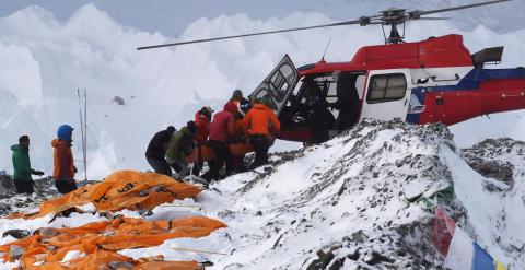 Una persona herida es subida a un helicóptero de rescate en el campamento base del Everest mientras los cadáveres de montañeros esperan ser trasladados, envueltos en sacos naranja.- AFP PHOTO / ROBERTO SCHMIDT