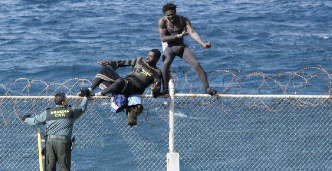 Dos inmigrantes intentan saltar la valla de Ceuta frente a un guardia civil. / Reduan (EFE)
