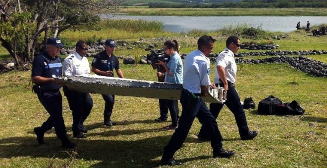 Varios agentes cargan con el fragmento supuestamente de avión hallado junto a la isla Reunión, en el Océano Índico. - AFP