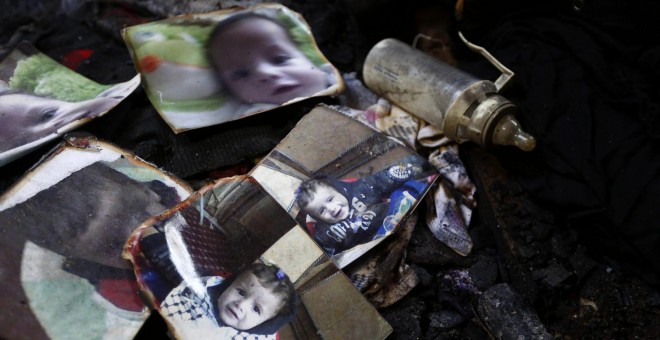 Un biberón descansa junto a las fotografías del bebé palestino de 18 meses Ali Dawabsha, que murió en un incendio provocado por colonos extremistas israelíes, entre los restos calcinados de su casa en la población palestina de Douma, junto a Nablus, 31 de