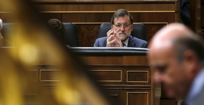 El presidente del Gobierno, Mariano Rajoy, observa al ministro de Economía, Luis de Guindos, durante su intervención en el pleno del Congreso.- REUTERS