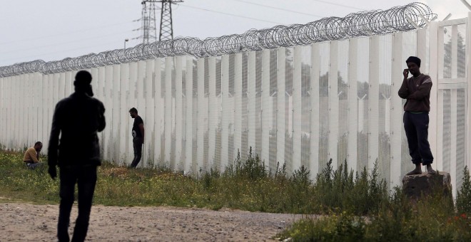 Varios inmigrantes llaman por teléfono cerca de una cerca con alambre de púas, junto al campamento improvisado llamado 'La nueva jungla' en Calais, Francia.- REUTERS / Regis Duvignau