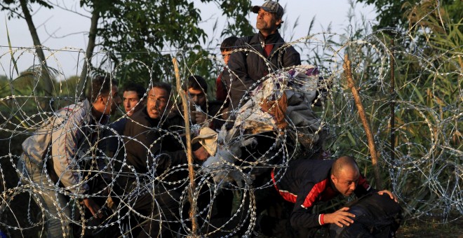 Refugiados sirios cruzan la valla de cuchillas que Hungría ha instalado en su frontera con Serbia, cerca Röszke.- REUTERS / Bernadett Szabo