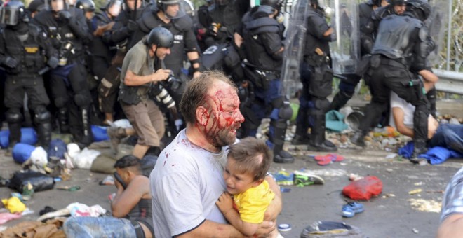 Un migrante herido sostiene a un niño durante los disturbios con la policía húngara en la frontera con Serbia. REUTERS