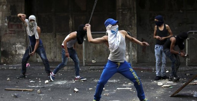 Varios palestinos lanzan piedras durante los enfrentamientos registrados con policías israelíes en la ciudad cisjordana de Hebrón.