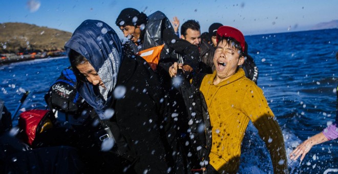 Refugiados y migrantes reaccionan al llegar en un bote a la isla griega de Lesbos, después de cruzar el mar Egeo desde Turquía, el 15 de octubre de 2015. AFP/DIMITAR DILKOFF