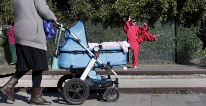 Una madre empuja el cochecito en el que lleva a su hijo, cerca de un anciana que practica Taichí en Pakín. REUTERS/Jason Lee