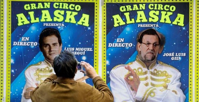 Un hombre toma una fotografía de los carteles de un circo que actúa estos días en Valencia y en los que alguien ha sustituido las caras de dos de sus artistas por los candidatos a la presidencia del Gobierno Albert Rivera y Mariano Rajoy./ EFE