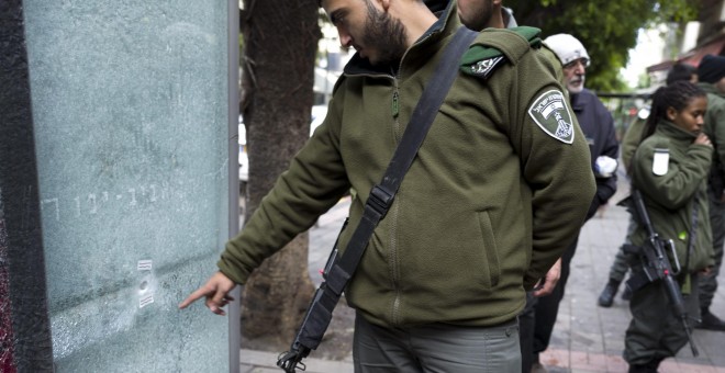 Un agente de policía de fronteras israelía señala uno de los agujeros de bala producido por los disparos de un árabe-israelí que mató el viernes a dos personas e hirió a siete en un pub de Tel Aviv. EFE/EPA/JIM HOLLANDER