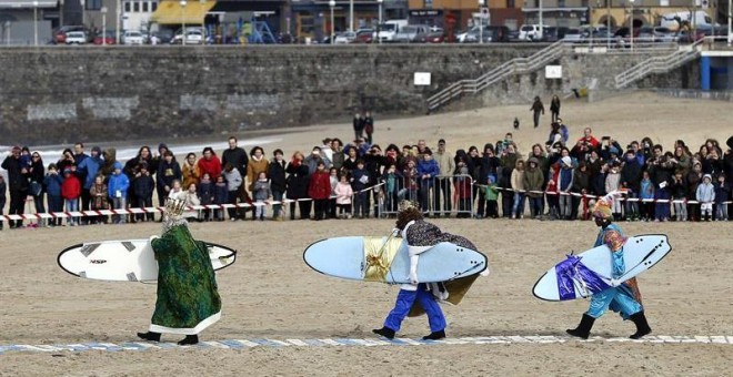 Los Reyes Magos con sendas tablas de surf a su llegada hoy a la donostiarra playa de La Zurriola. EFE/Javier Etxezarreta