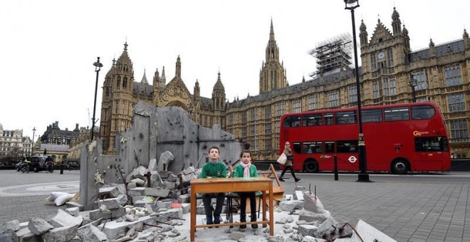 Dos pequeños sirios se sientan en un pupitre instalado en una recreación de su colegio bombardeado en Alepo (Siria) a las puertas del Parlamento en Londres (Reino Unido) durante un evento organizado por Save the Children para concienciar sobre la importan