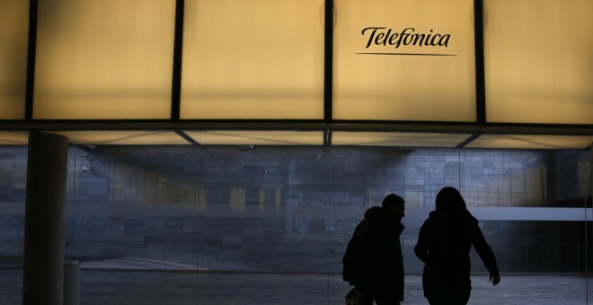 Dos personas pasan bajo el logo de Telefónica en la sede de la operadora en el distrito de Las Tablas de Madrid. REUTERS/Juan Medina