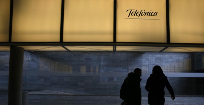 Dos personas pasan bajo el logo de Telefónica en la sede de la operadora en el distrito de Las Tablas de Madrid. REUTERS/Juan Medina