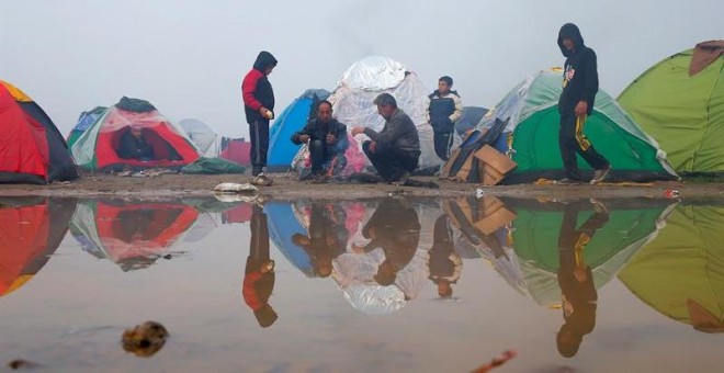 Refugiados se calientan junto a una hoguera improvisada en el campo de refugiados en la frontera griega y macedonia cerca de Idomeni (Grecia). - EFE