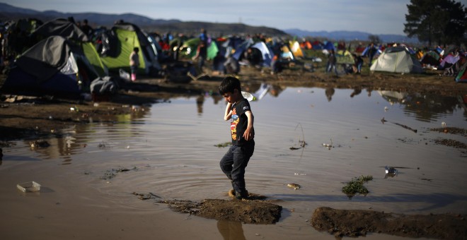Un niño lleva una botella de agua mientras camina por el barro, a la espera de cruzar la frontera entre Grecia y Macedonia, en un campamento improvisado para los migrantes cerca del pueblo de Idomeni. REUTERS/Stoyan Nenov