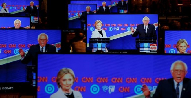 Hillary Clinton y Bernie Sanders aparecen en varias pantallas durante su último debate. - EFE