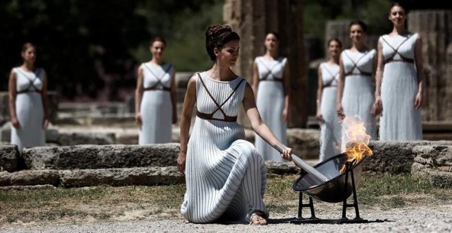 La actriz griega Katerina Lehú (d), en el papel de la Gran Sacerdotisa de Olimpia, enciende la llama mediante un espejo parabólico que desvía los rayos solares hacia la antorcha. /EFE