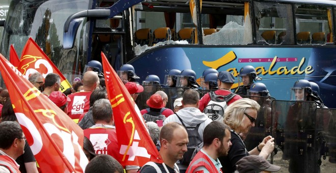 Los trabajadores franceses del sindicato CGT pasan junto a los gendarmes franceses que se interponen en línea cerca de un autobús con las ventanas rotas tras los enfrentamientos con manifestantes durante una manifestación en París como parte de las protes