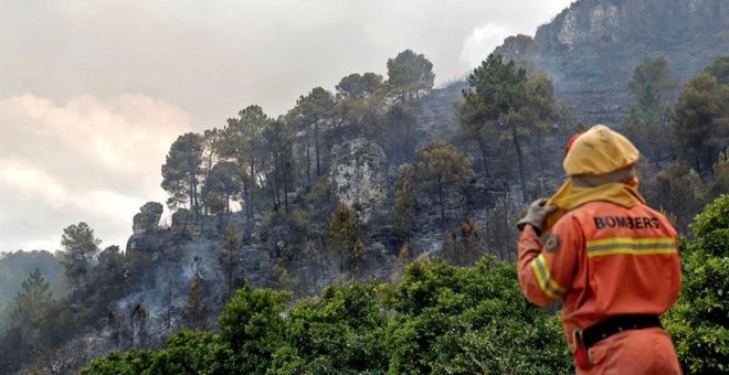 Una bombera observa el frente del incendio forestal en la localidad de la Barraca de Aguas Vivas (Valencia). Cuatro incendios forestales afectan a una decena de municipios en Valencia, el más preocupante en Carcaixent, donde han sido evacuados los pacien