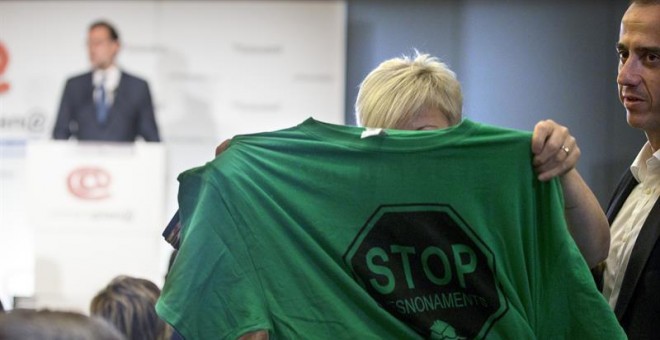 Una activista de la PAH muestra una camiseta alusiva a los desahucios durante intervención de Rajoy en Barcelona./ EFE