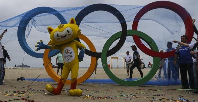 Vinicius, la mascota de los Juegos de Río, posa junto a la escultura de los anillos olímpicos. - EFE