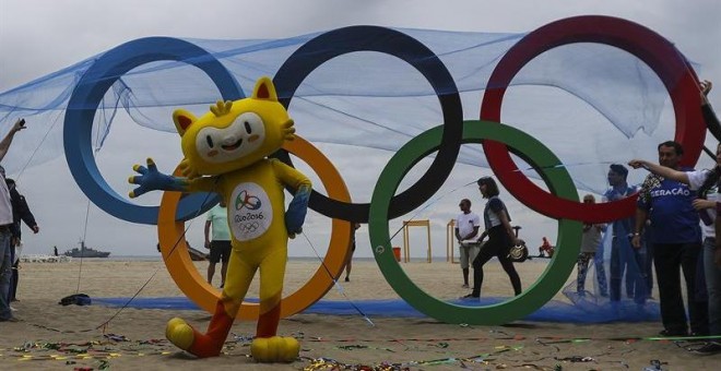 Vinicius, la mascota de los Juegos de Río, posa junto a la escultura de los anillos olímpicos. - EFE