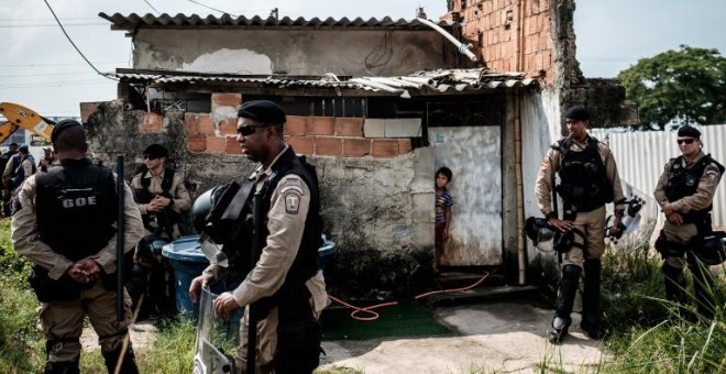 Un niño se asoma, en presencia de la Policía, por la puerta de su casa después de que la de sus vecinos fuera demolida en el barrio de Vila Autódromo, en Río de Janeiro. - AFP