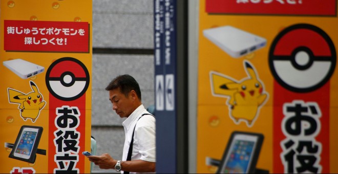 Un hombre utiliza su teléfono móvil enfrente de un anuncio con la imagen del juego Pokémon GO en una tienda de Tokio, Japón. REUTERS/Kim Kyung-Hoon