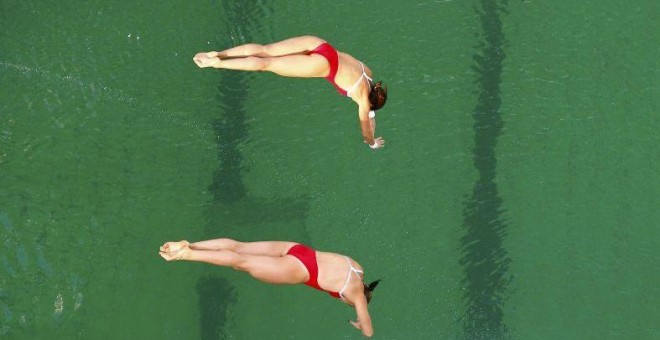 Dos nadadoras realizan un salto durante la competición desarrollada en la piscina con el agua de color verde.- REUTERS