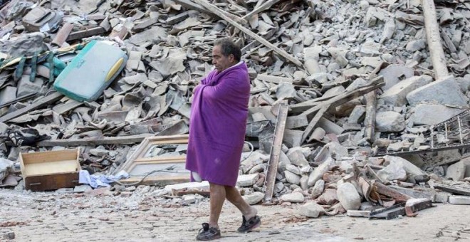 Un hombre que acaba de ser rescatado pasea entre los escombros de la que era su casa/REUTERS