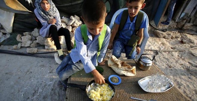 Niños palestinos desayunan antes de ir al colegio en la localidad cisjordana de Susiya. Los alumnos caminan un largo recorrido hasta el colegio debido a la falta de infraestructuras y a la prohibición de Israel de construir un centro educativo. - EFE