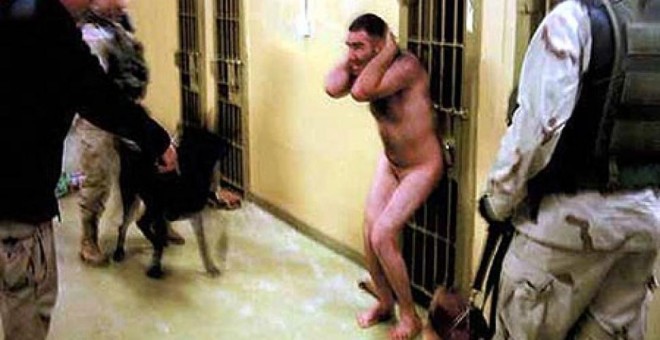 Un prisionero iraquí detenido por militares estadounidenses se encoge bajo de la amenaza de dos perros en la tristemente célebre prisión de Abu Ghraib. Las fotos de militares desvelaron los malos tratos y vejaciones a los detenidos en esa prisión.- AFP
