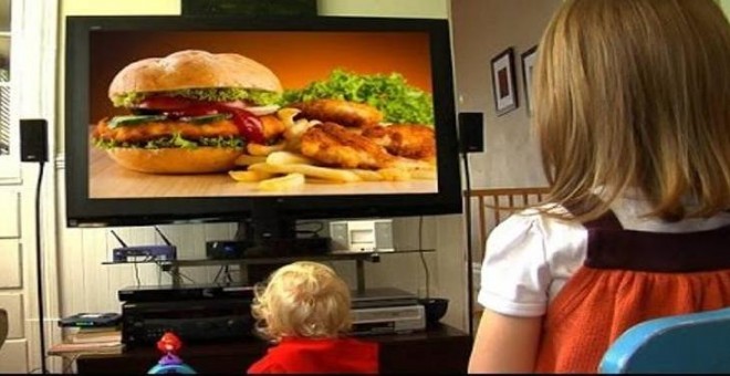 Niños viendo en la televisión un anuncio de comida poco saludable.