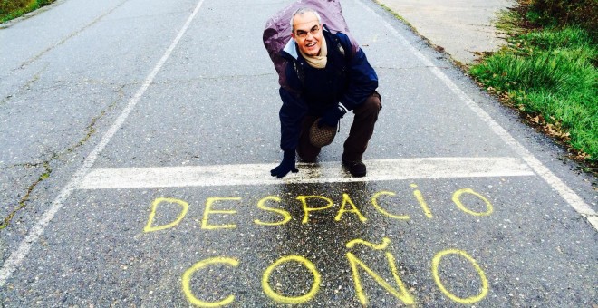 Susaeta posando en una carretera señalando una pintada en la que se lee 'Despacio coño'.
