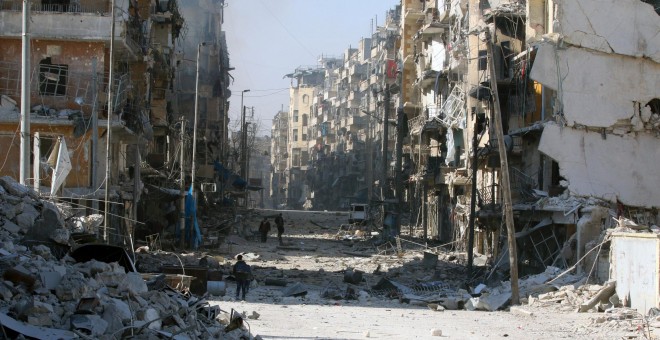 Varias personas andan por una calle del este de Alepo destrozada por los bombardeos. - REUTERS
