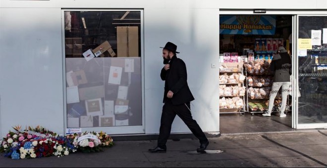 Un hombre camina junto a unas flores colocadas ante el supermercado judío Hyper Cacher. / IAN LANGSDON (EFE)