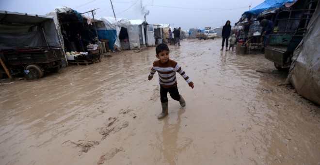 Un niño anda entre el barro en un campamento de desplazados sirios junto a la frontera con Turquía. - REUTERS
