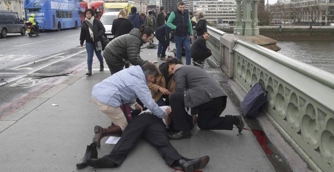 Varias personas atienden a uno de los heridos en el puente frente al Parlamento / REUTERS