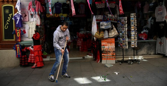 El empleado de una tienda de objetos turísticos del centro de Madrid barre la acera. REUTERS/Susana Vera
