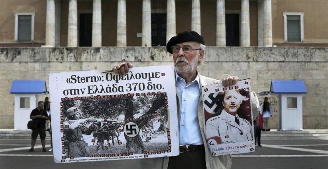 Un hombre sostiene un cartel de la canciller Angela Merkel como si fuera un miembro del partido nazi frente al Parlamento griego en la marcha por el Día de los Trabajadores en Atenas. /EFE