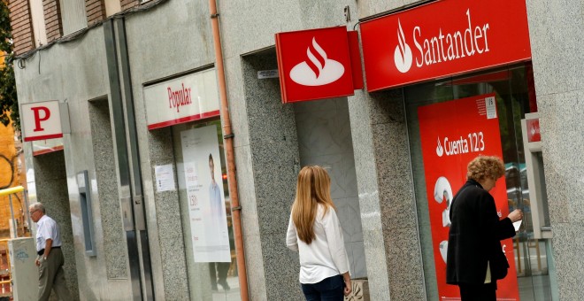 Un par de personas utilizan un cajero automático de una oficina del Banco Santander, en Barcelona, situada junto a una sucursal del Popular. REUTERS/Albert Gea
