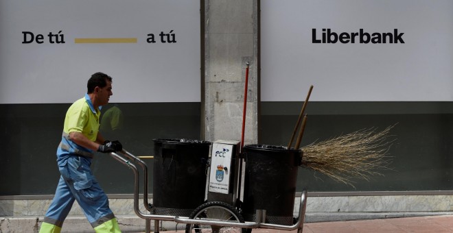 Un barrendero camina frente a una oficina de Liberbank en Oviedo. REUTERS/Eloy Alonso