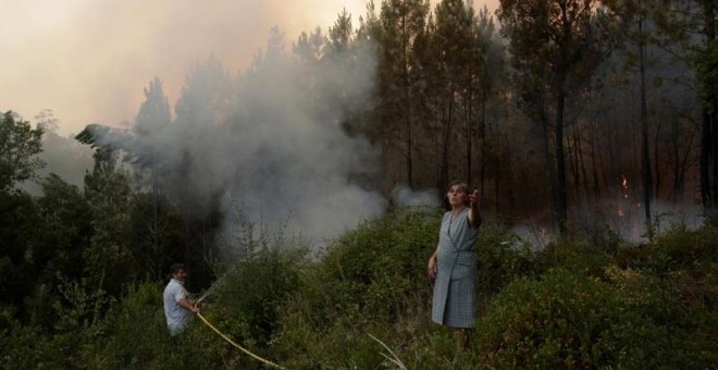 Dos habitantes de Louriceira intentan apagar un foco cerca de su pueblo. | MIGUEL VIDAL (EFE)