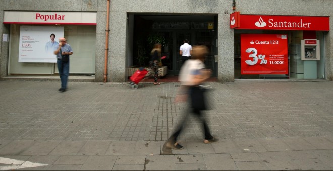 Varios personas pasan junto a sendas oficinas de Banco Popular y Banco Santander, en Barcelona. REUTERS/Albert Gea