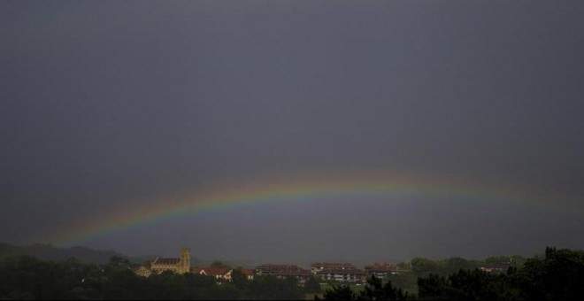 Vista de un arco iris sobre el cielo negro de San Sebastián, donde aún este viernes se mantiene la alerta amarilla por fenómenos costeros. | EFE