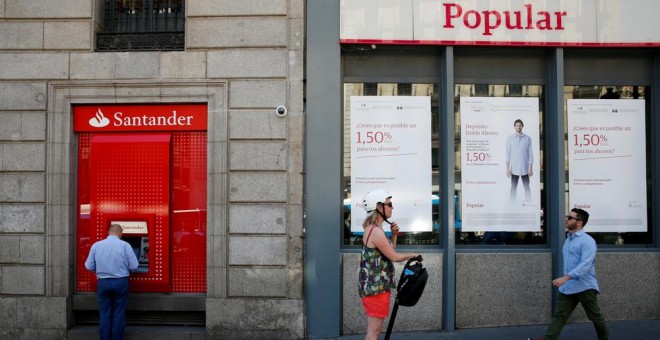 Un hombre utiliza un cajero automático del Banco Santander junto a una oficina del Popular, en Madrid. /Juan Medina