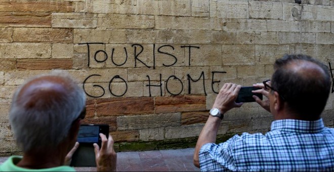 Dos personas toman una foto de una pintada contra el turismo en el centro histórico de Oviedo. REUTERS/Eloy Alonso