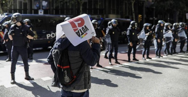 Una persona con un cartel en favor del Sí en el referéndum del 1-0 pasa delante de los antidisturbios de la Policái Nacional desplegadas ante la se sede del CUP. | XAVI HERRERO