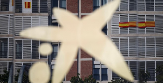 El logo de Caixabank, en su sede de Barcelona, donde se reflejan los edificios vecinos con banderas españolas y catalanas. REUTERS/Albert Gea